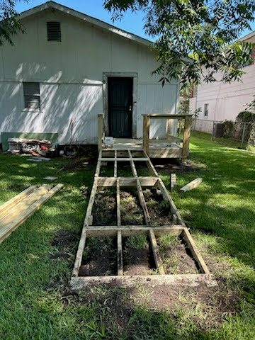 The skeleton of a long wooden ramp framed out across a back yard, running from the new landing down to the grass.